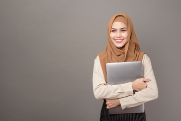 Portrait of beautiful woman with hijab is holding computer laptop on gray background