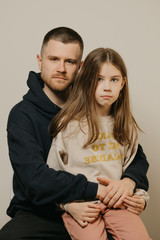 A young serious father with a beard hugs strongly his cute daughter. A child with long hair sitting on daddy's lap. Family photo..