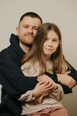  A young happy father with a beard hugs strongly his cute daughter. A child with long hair sitting on daddy's lap. Family photo.