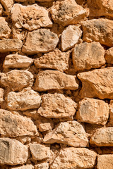 Old rustic man-made Spanish sand stone wall using only natural materials. The wall is in a bad condition and has been aged and dried out by the sun over the years.