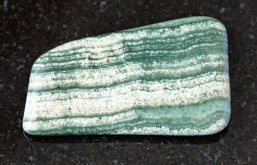 closeup of sample of natural mineral from geological collection - tumbled Skarn rock on black granite background from Bora quarry, Primorye, Russia