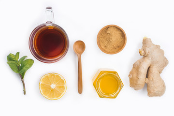 A glass cup of black natural tea with ginger, lemon, mint and honey isolated on wooden white rustic background. Healthy vitamin drink.