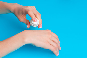 Female hand holding skincare product bottle on blue