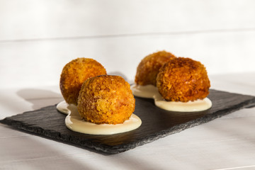 Fried meat balls or croquettes with white sauce on black stone plate on white wooden background. Unhealthy food. Traditional spanish snack.