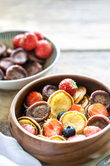 Tiny pancake cereal and chocolate mini pancakes in a wooden bowl on a wooden table. Copy space