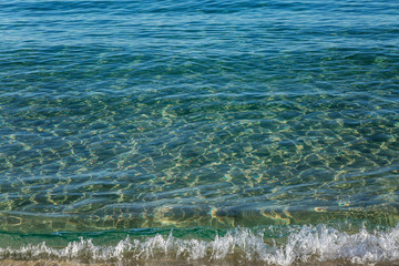 Turquoise foamy wave on a golden sandy shore. The calm surface of the sea. Relax and tranquility. Background. Space for text.