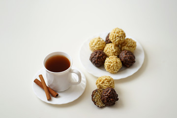 sweet round chocolate and yellow dessert are on a plate, one piece in a cut, a Cup of tea with cinnamon on a saucer, on a white table
