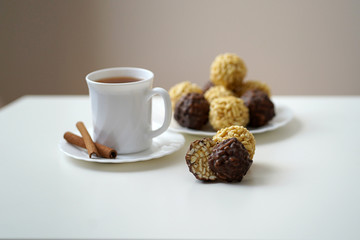 a Cup of tea with cinnamon on a plate on a white table with a sweet dessert on a plate, round shape of chocolate and yellow color