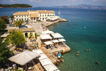 Naklejka premium CORFU, GREECE - 10.09.2019 - Faliraki beach Alecos Baths public bathing spot with rock and pier ans restaurant in Corfu Town, Ionian Sea