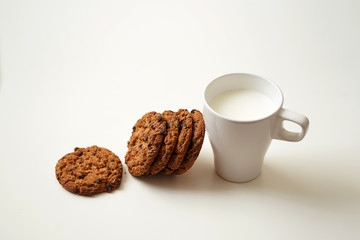 oatmeal round cookies are leaning sideways against a mug with a mug of milk, a full Cup of milk, one cookie lying next to it