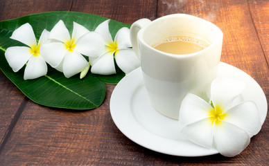 Cup of coffee with white frangipani flower on wood