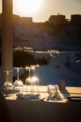 Restaurant table decorated with glasses on terrace in sunset light on the island Santorini, Cyclades, Greece
