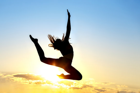 Graceful gymnast dancer jumping leaps against sunset