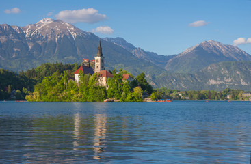 Sunny morning at Lake Bled and Julian Alps in the background. The lake island and charming little church dedicated to the Assumption of Mary are famous tourist attraction in Slovenia