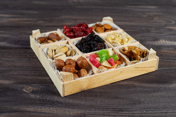 Assorted dried fruits and nuts in a wooden box isolated on a dark wood background. Raisins, candied fruits, cherries, Brazil nuts, hazelnuts, walnuts, almonds, cashews, pistachios.