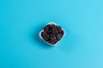 A portion of black raisins in a paper muffin cup on a blue background.
