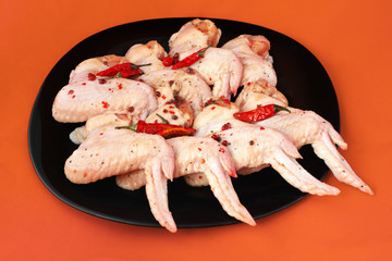raw chicken wings with spices, pickled with hot pepper, on black plate, bright background