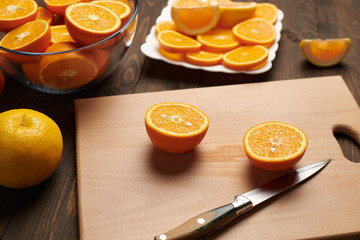 Fresh orange fruit whole and sliced on a wooden table, cutting board and kitchen knife. A plate full of citrus slices - natural and healthy food. Glass of fruit cocktail.