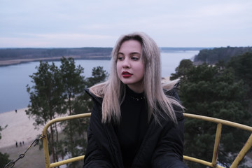 Fototapeta premium Young blonde girl rides on rusty ferris wheel at spring