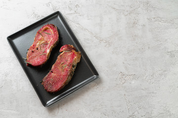 Two fresh raw meat steaks on black ceramic plate