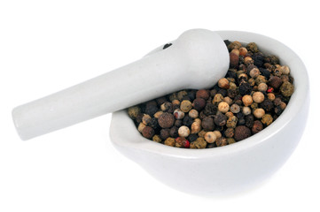Poivre en grains dans un mortier avec un pilon en gros plan sur fond blanc