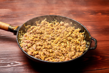 Grilled minced meat with onions, spices and cream in a pan on a dark wooden background. Cooking toppings.