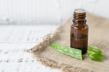 Aloe vera oil in a dark glass bottle on a white wooden table and wooden background