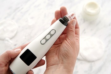 Vacuum blackhead remover in woman hands, modern face skin cleaning.