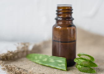 Aloe vera oil in a dark glass bottle on a white wooden table and wooden background