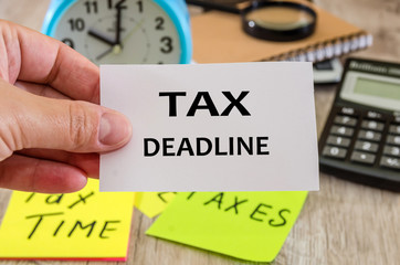 A sheet of paper with the text TAX DEADLINE in hand on the background of a calculator and alarm clock. Tax concept. Close-up.