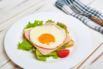 Toast with ham, egg and tomato on a plate on a light wooden background.