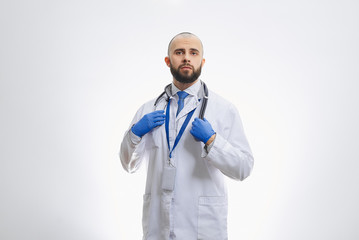 A doctor with a stethoscope and disposable medical gloves. A bald physician with a beard preparing to examine patients.