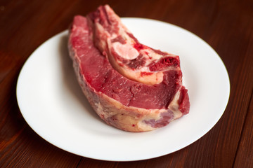 Raw veal steak on a white plate on a wooden background.