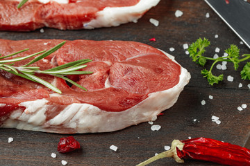 Raw meat steaks with herbs on wooden board