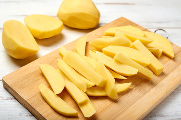 Sliced potato on a cutting board on a light wooden background. Preparing potatoes for cooking.