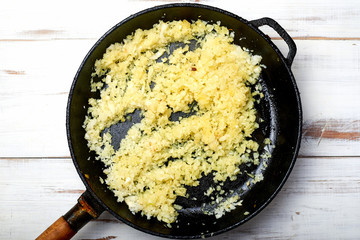 Fried onions in a pan on a light wooden background. Preparation for cooking.