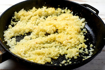 Fried onions in a pan on a light wooden background. Preparation for cooking.