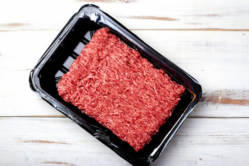 Minced meat in packaging on a light wooden background.