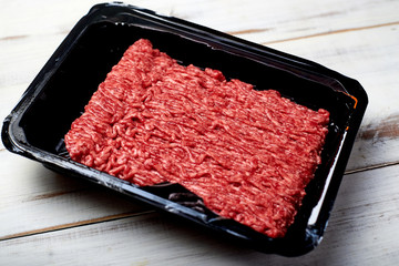 Minced meat in packaging on a light wooden background.