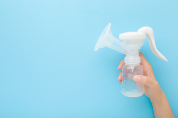 Young mother hand holding plastic breast pump bottle on light blue table background. Pastel color....