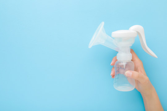 Young Mother Hand Holding Plastic Breast Pump Bottle On Light Blue Table Background. Pastel Color. Closeup. Preparing Milk For Baby Feeding. Empty Place For Text. Top Down View.