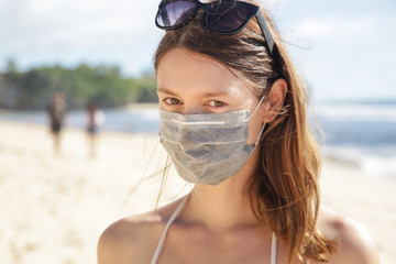 Woman wearing protective face mask on the beach. Summer vacation after Coronavirus pandemic crisis.