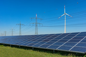 Solarpark mit Hochspannungsleitung und Windrad vor blauem Himmel Konzept erneuerbare Energie