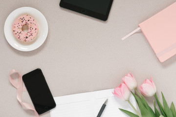 Trendy stylish frame for a female blogger, freelancer: pink diary, tablet, phone, Donat on a plate, pink tulips and an open Notepad with a clean page on a coffee background with copy space. 