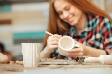 Young woman sculpting cup. Person is on the background. Product is in the front.