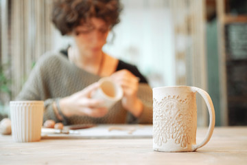 Pottery product with person on the background. Mug made out of clay.