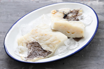 fresh raw cod fish with ice on dish on ceramic background