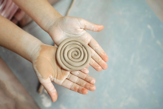 Kid's hands hold clay product. New hobby. Pottery workshop.