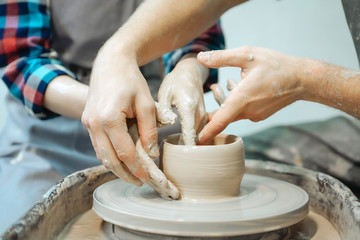Couple's hands making a pot. Date at the pottery workshop. Closeup picture.
