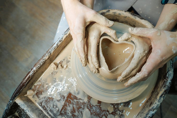 Couple hands making a pot in the shape of a heart. Date at the pottery workshop. Concept of love